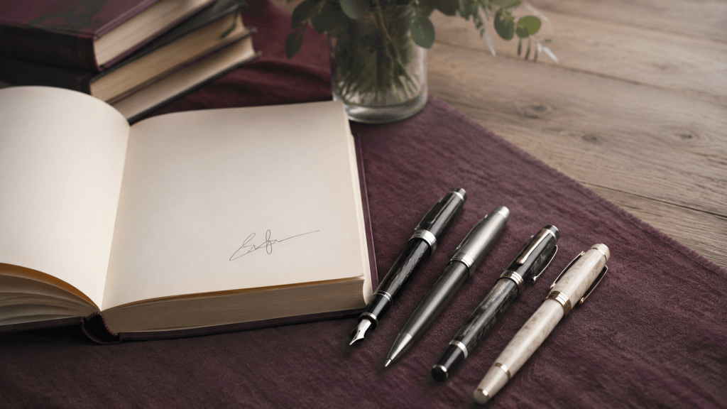 Four unbranded pens arranged beside an open novel on a warm book-signing table